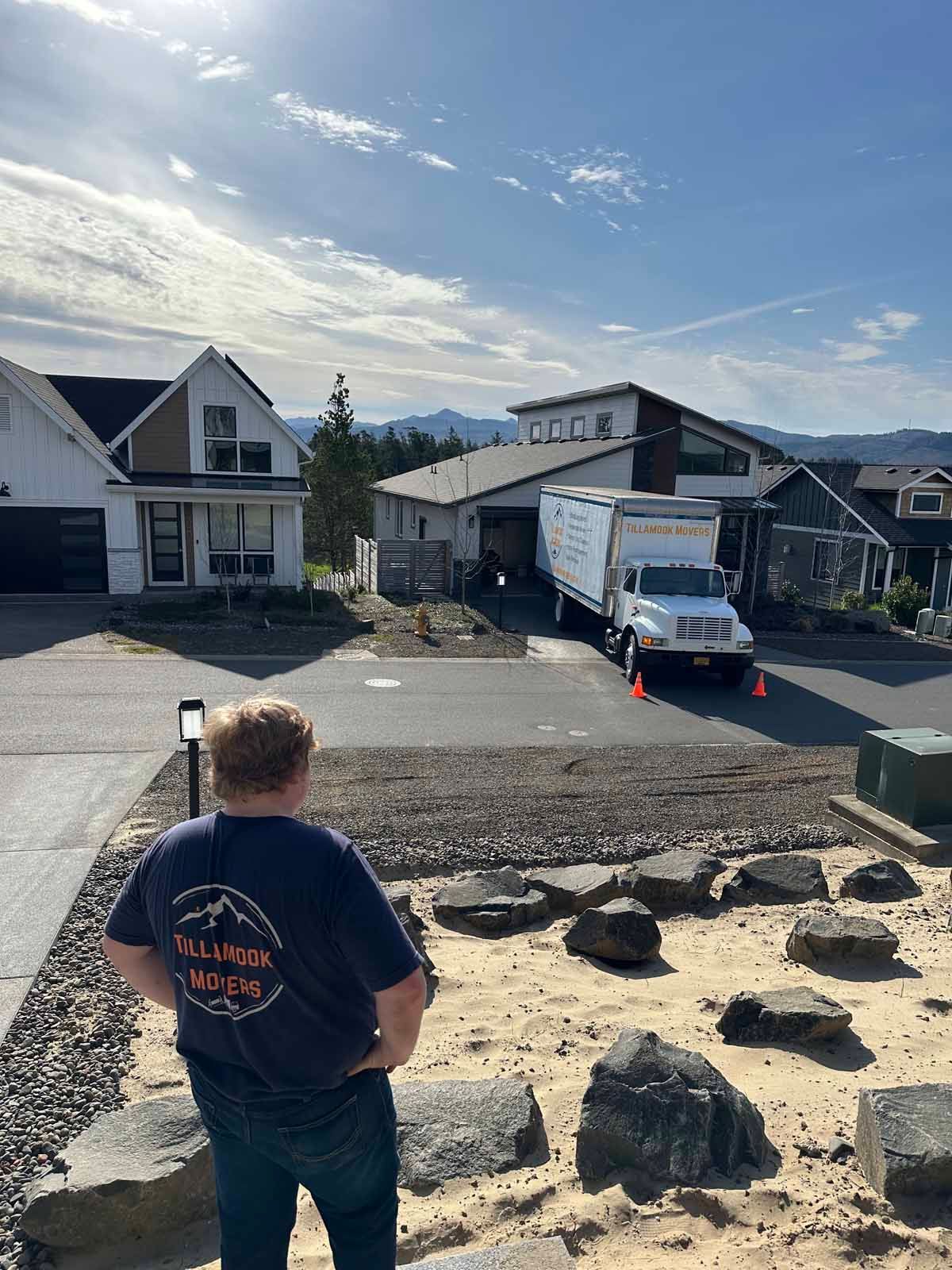 A man is standing in front of a house looking at a moving truck.