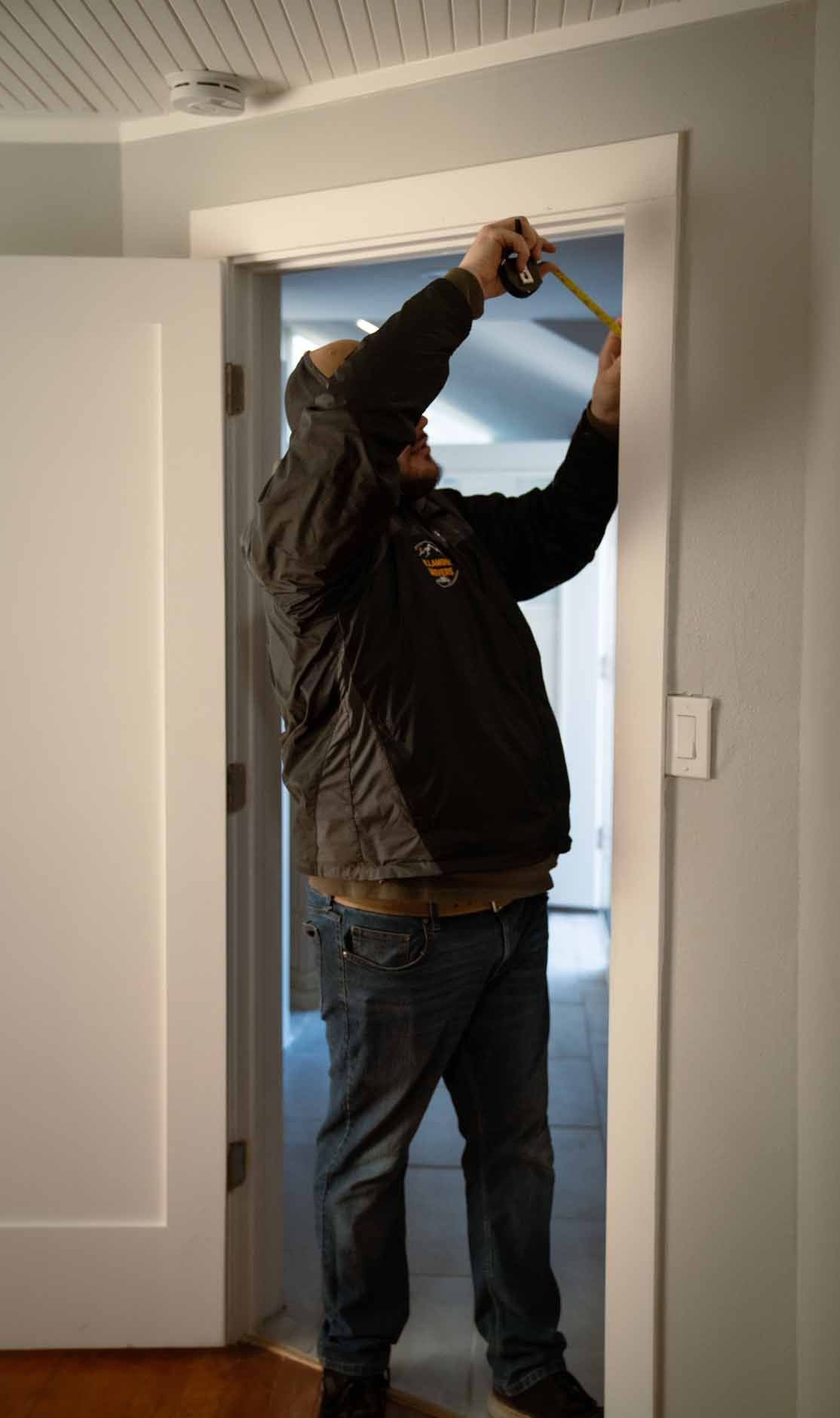 A man is measuring a door with a tape measure.