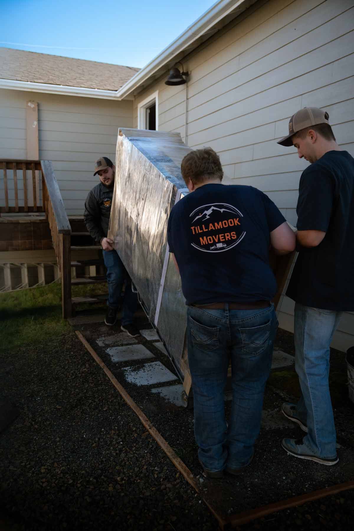 Three men are carrying a large piece of metal in front of a house.