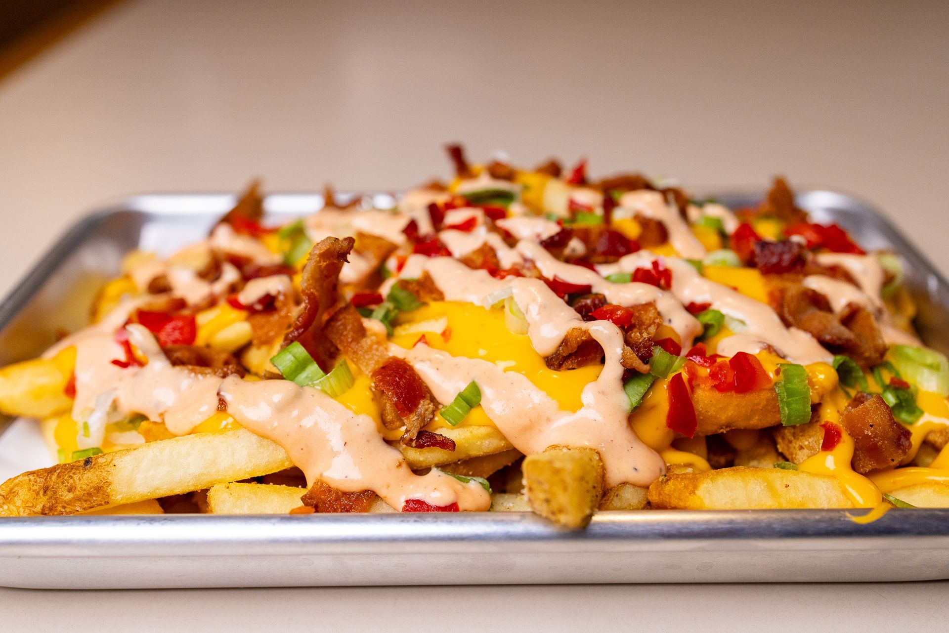 A tray of french fries with cheese , bacon and sauce on a table.