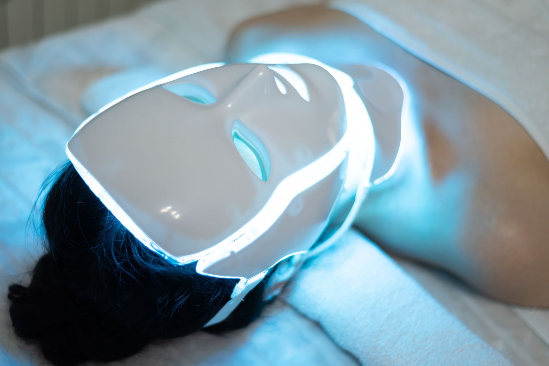 A person lying down while wearing a glowing blue light therapy mask.