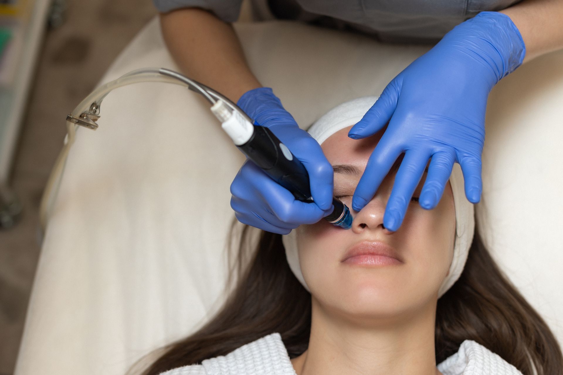 A provider in blue gloves uses a cosmetic suction device on a client's nose during a facial treatment.