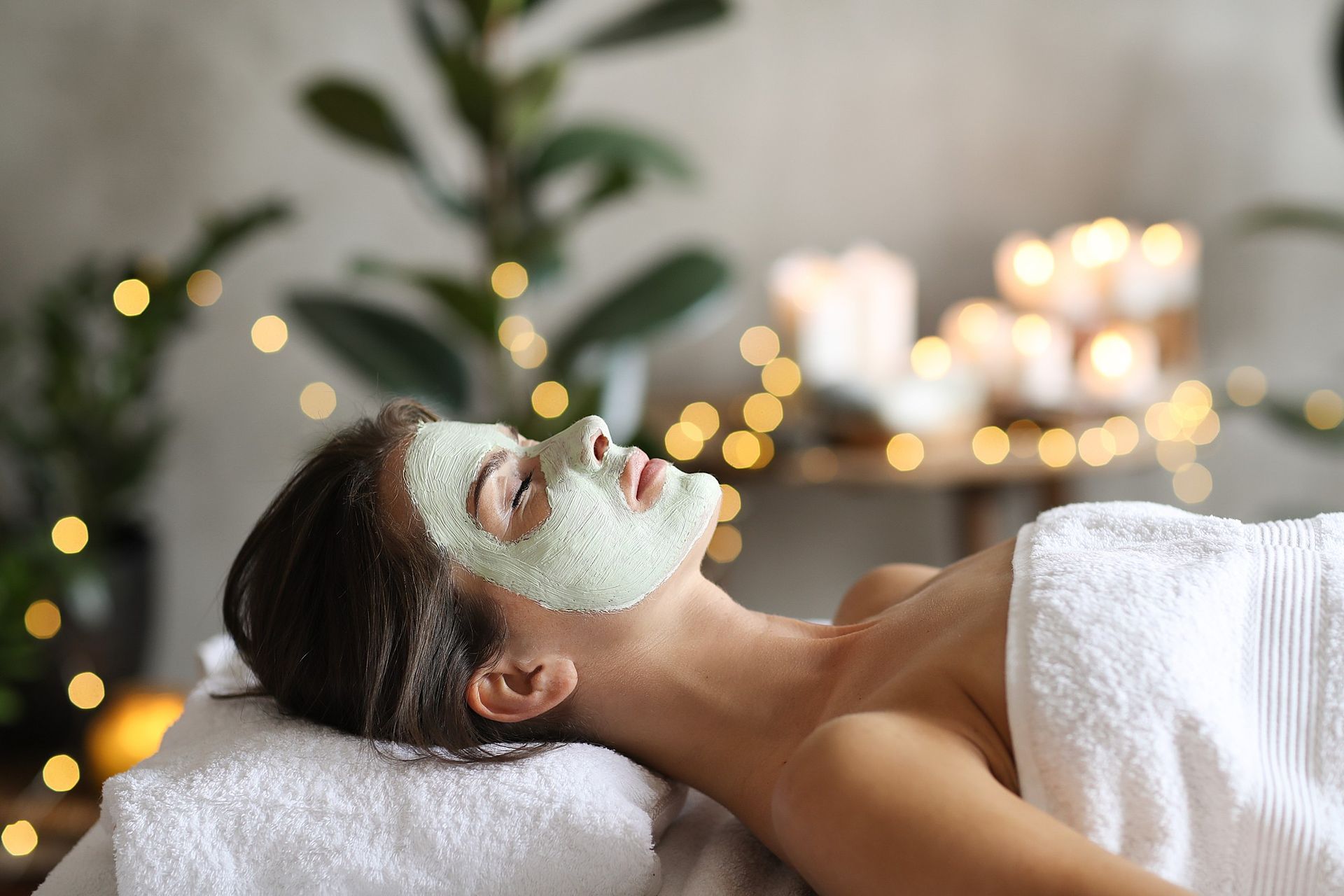 A woman is laying on a bed with a green mask on her face.