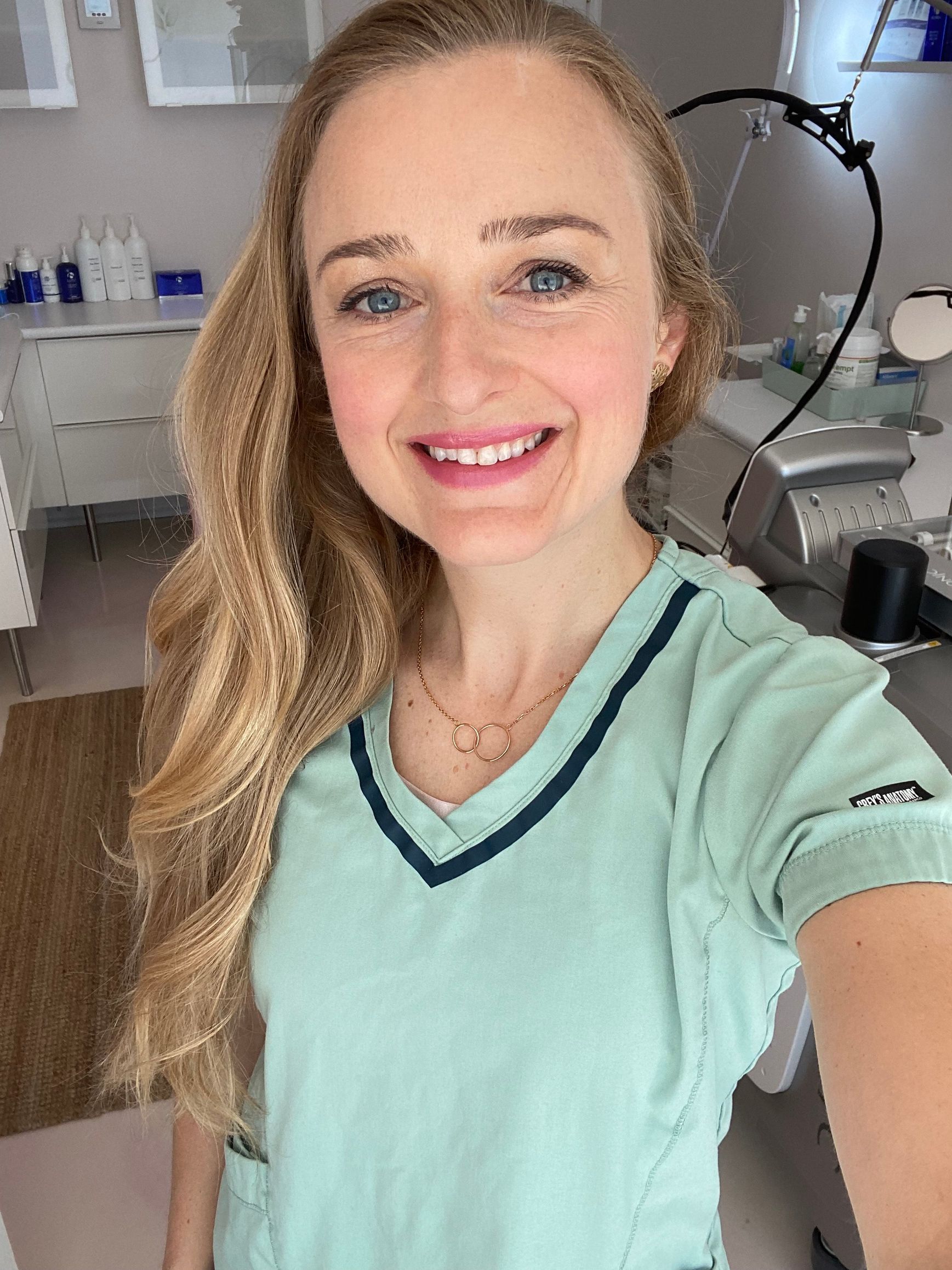 A woman in a scrub top is taking a selfie in a room.