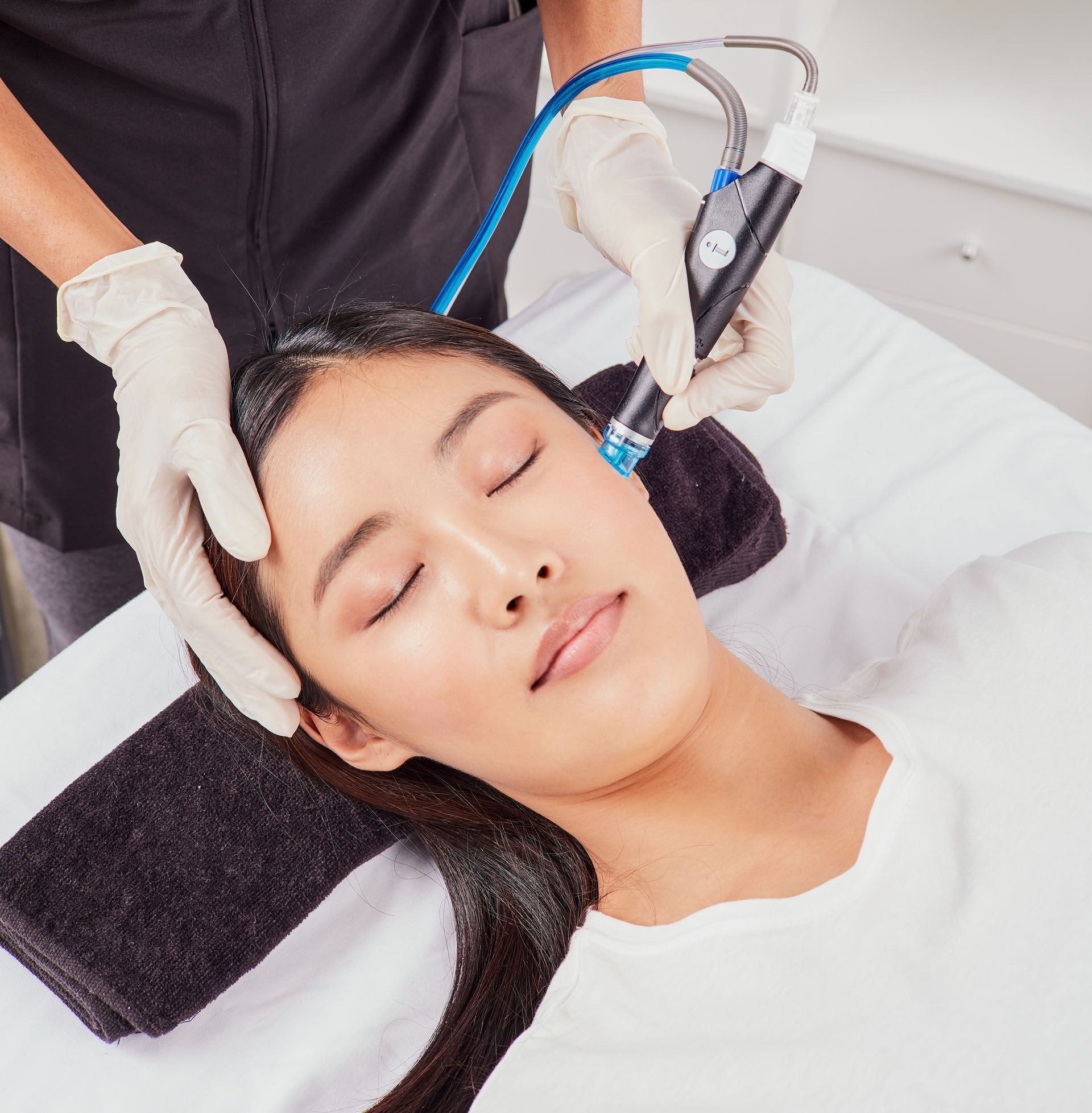 A woman receiving a facial treatment at a spa. A gloved person holds a device to her face.