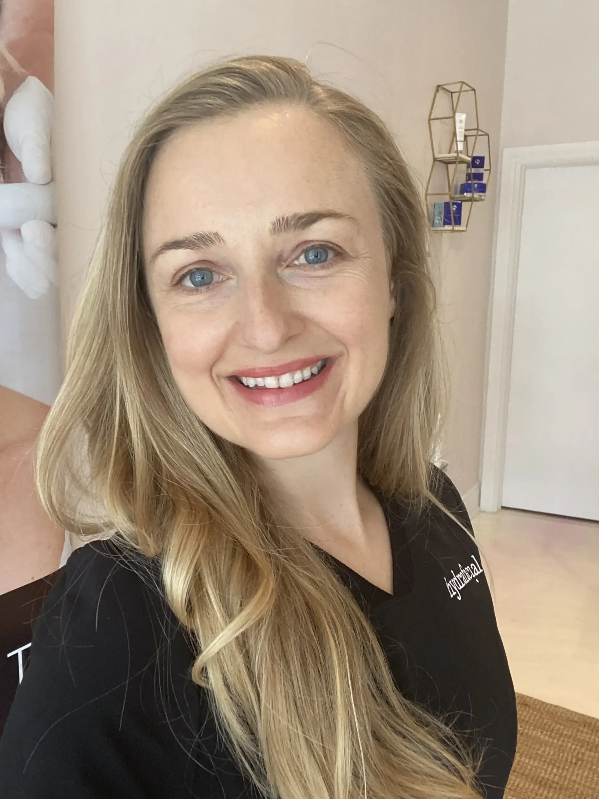 A woman with long blonde hair is smiling and wearing a black shirt.