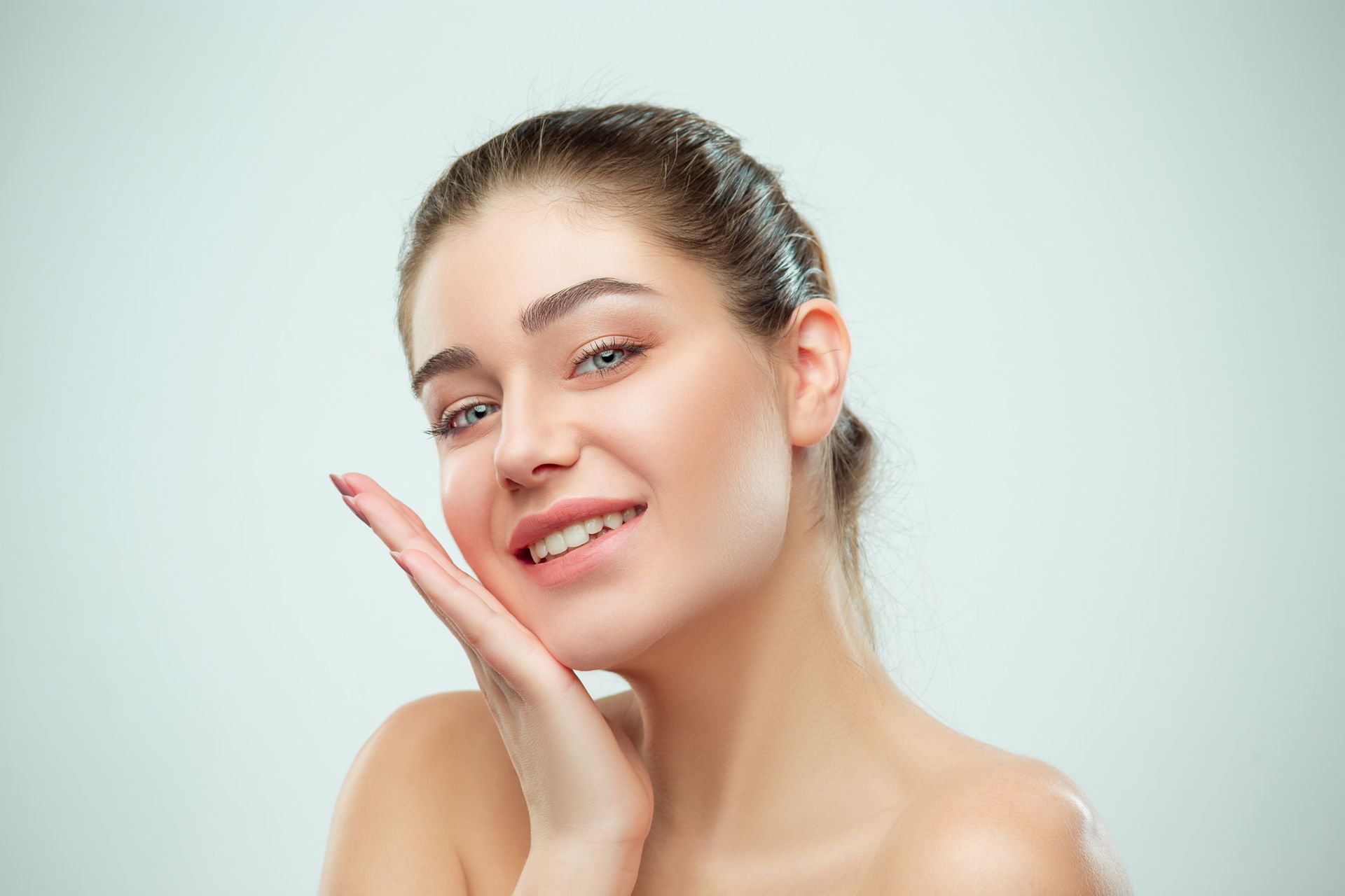 A woman is touching her face with her hand and smiling.