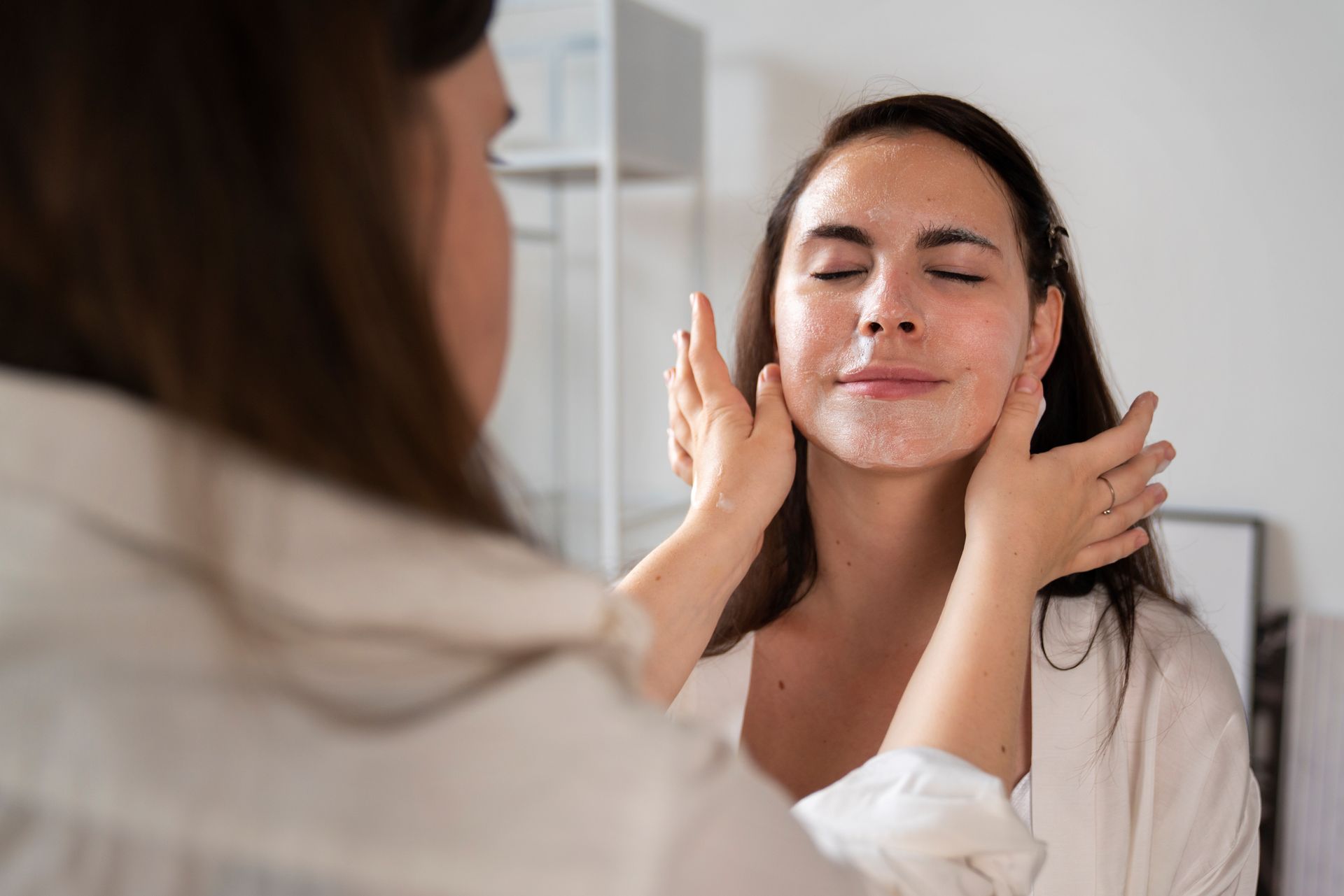 A woman is applying a cream to her face in front of a mirror.
