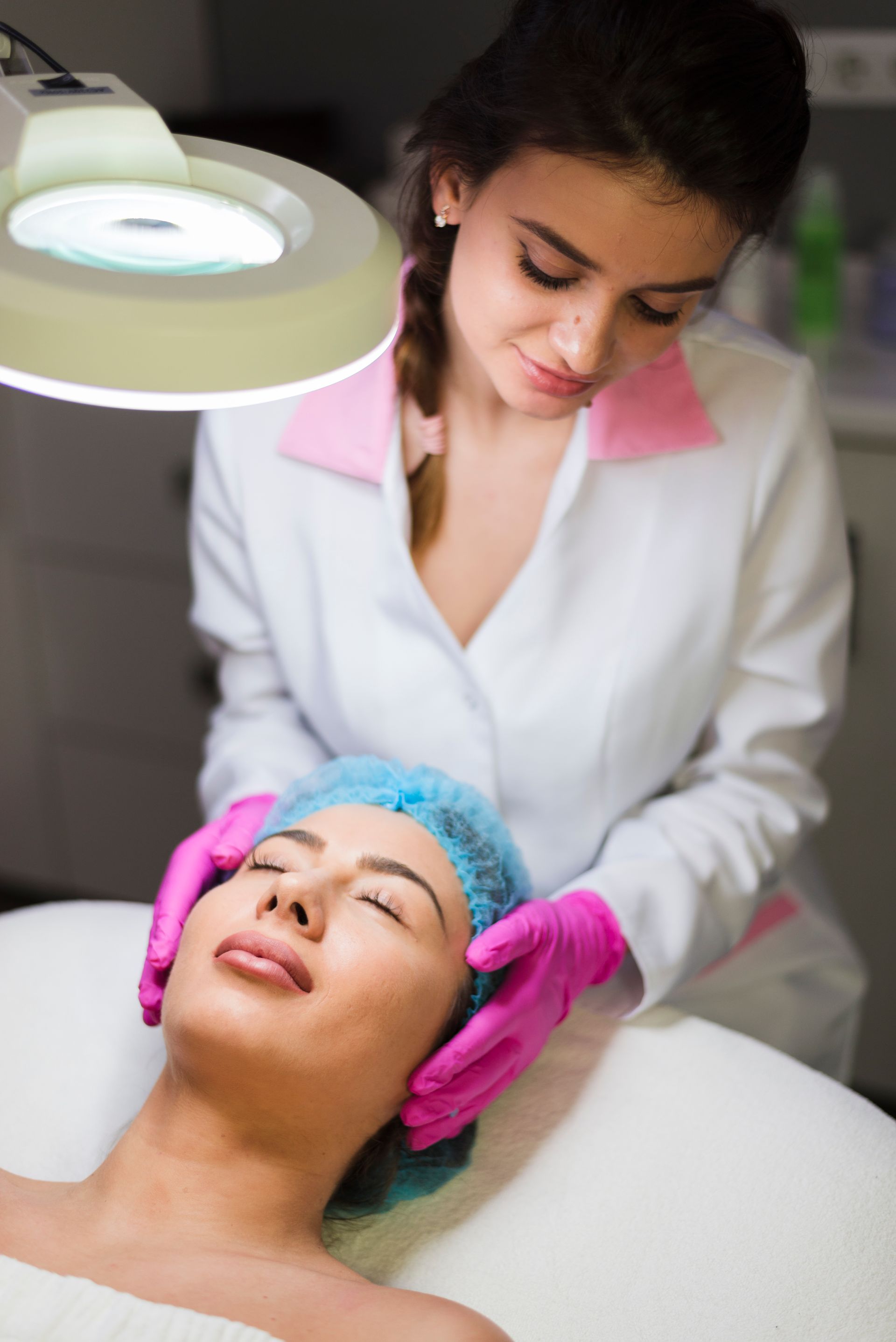A woman in pink gloves is examining a woman 's face with a magnifying glass.
