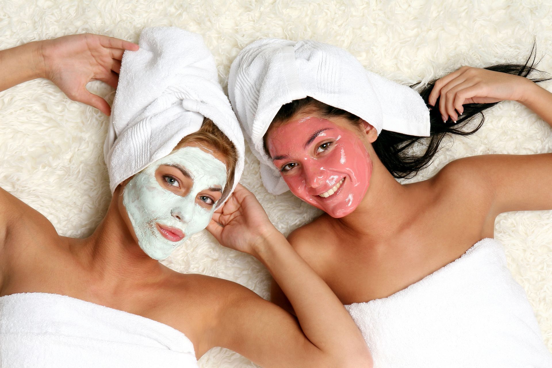 Two women are laying on a bed with facial masks on their faces.