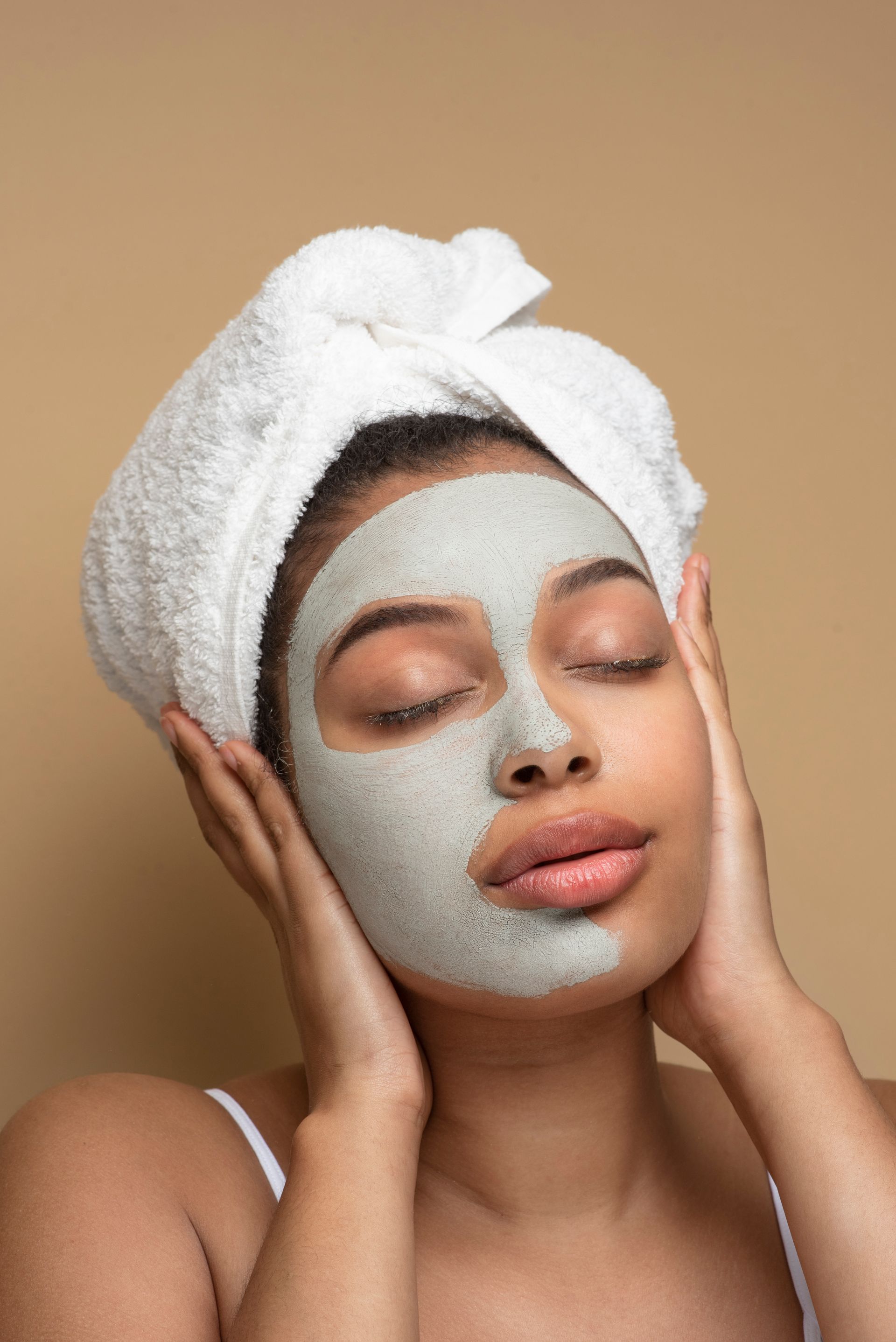 A woman with a towel wrapped around her head is wearing a clay mask on her face.