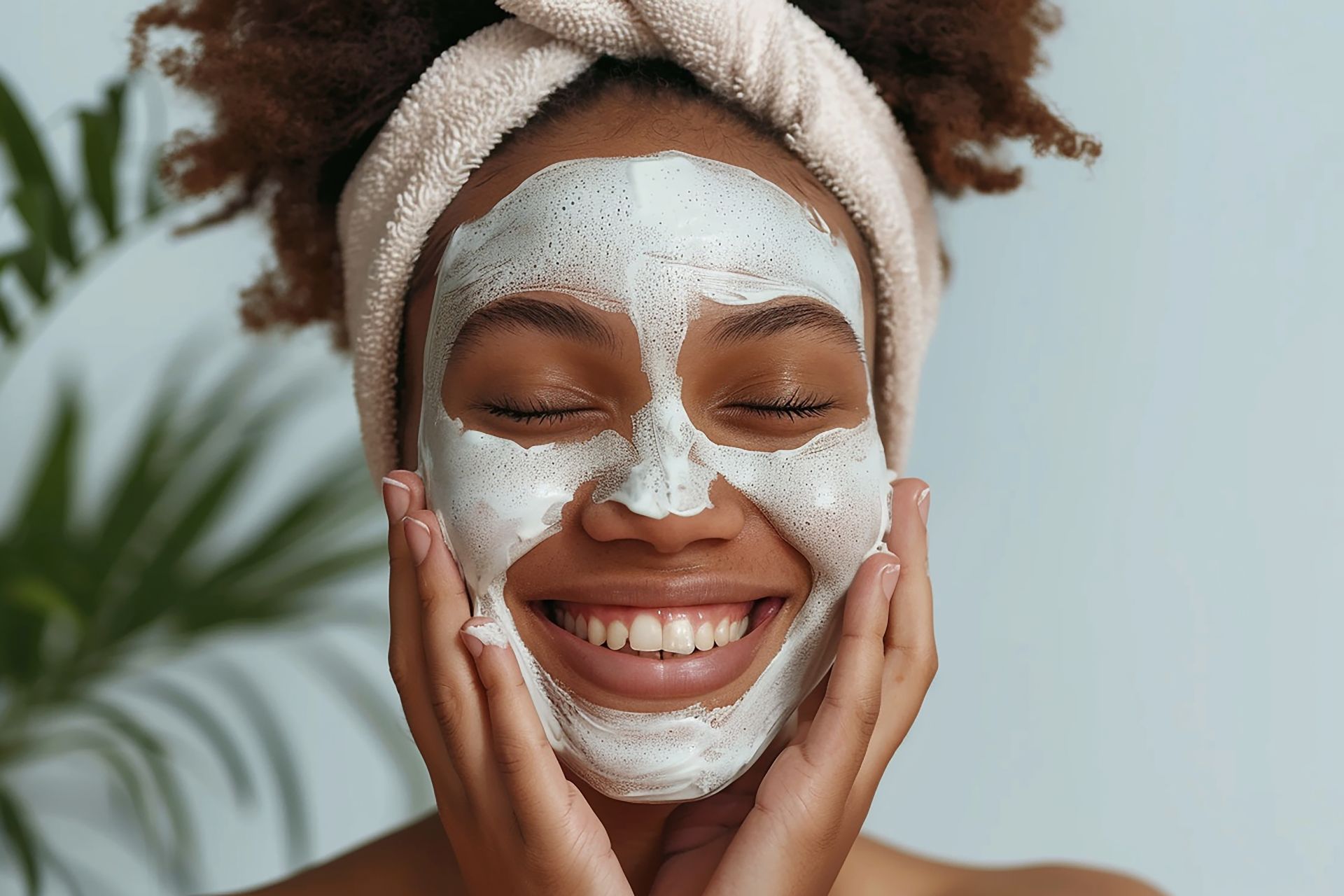 A woman with a towel wrapped around her head is smiling while wearing a face mask.