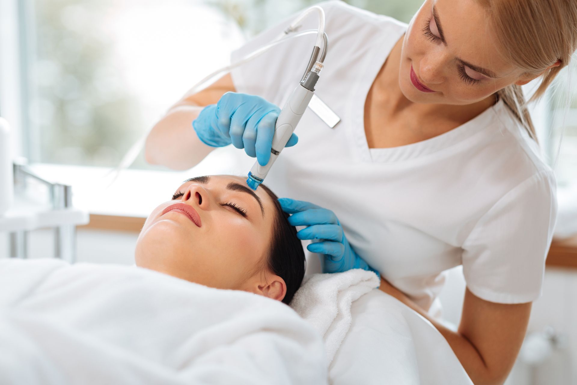 A professional providing a facial treatment using a handheld device on a client lying on a treatment table.