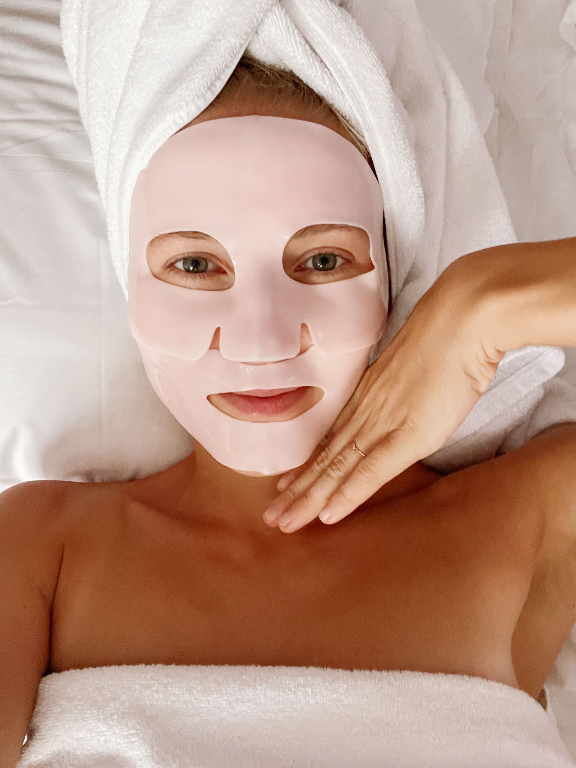 A woman with a towel wrapped around her head has a pink mask on her face