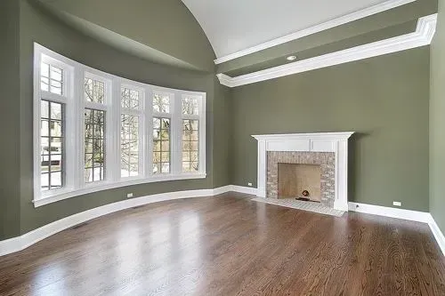 Empty room with curved window, fireplace, and hardwood floors. Walls are green, trim white.