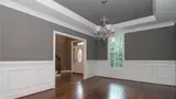 Empty dining room with gray walls, white trim, hardwood floors, and a chandelier.