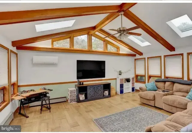 Living room with wood beams, skylights, tan sectional, TV, and light wood floors.