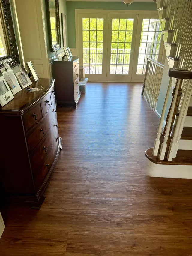 A hallway with wooden floors, two dressers, stairs, and French doors leading outside.
