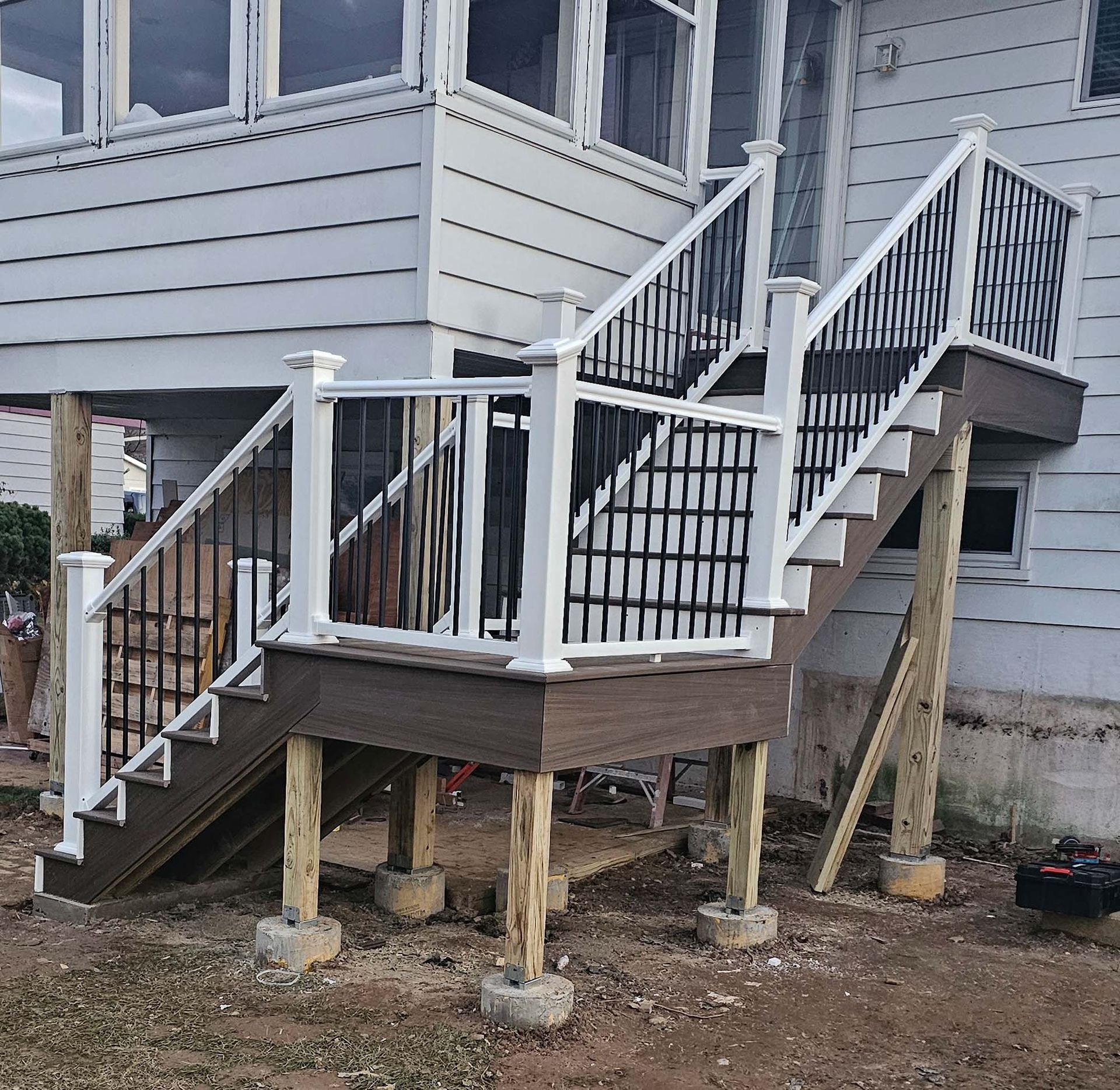 Exterior wooden staircase with composite decking and white railing, black balusters, and support posts.