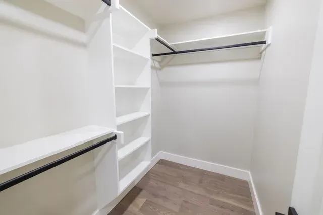 Empty white walk-in closet with shelves and hanging rods; wooden floor.