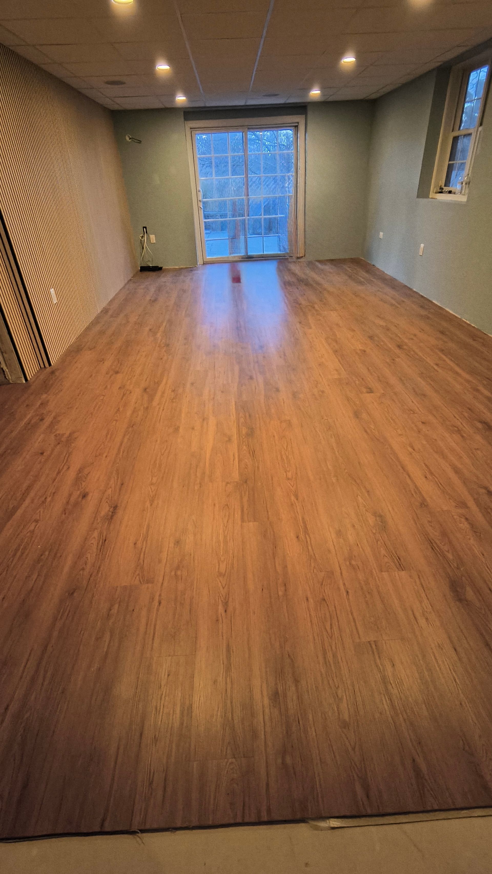 Empty room with brown wood-look flooring, light green walls, a sliding glass door, and recessed lighting.