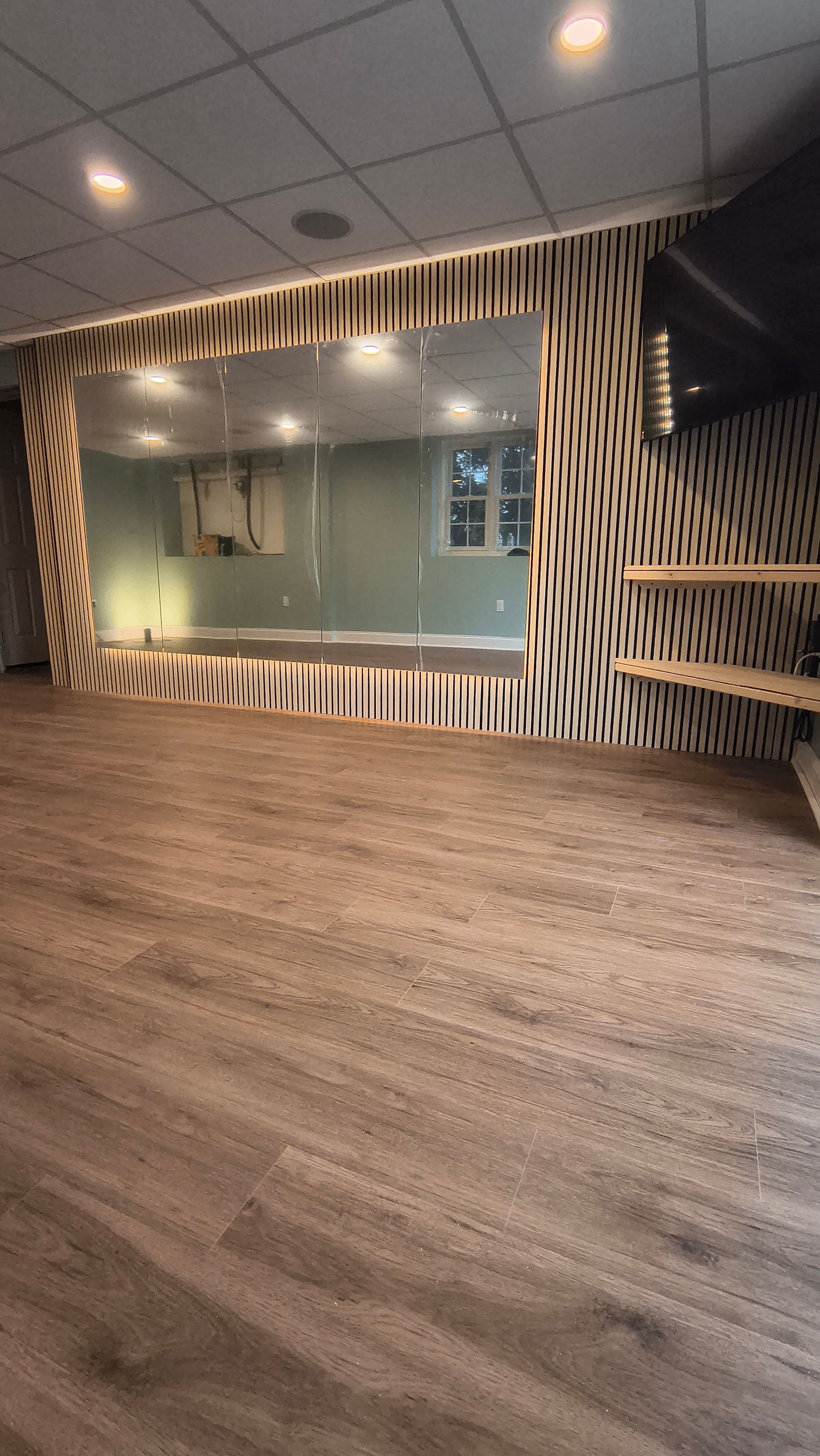 Empty room with wooden floors, a large mirror, and decorative wall paneling.