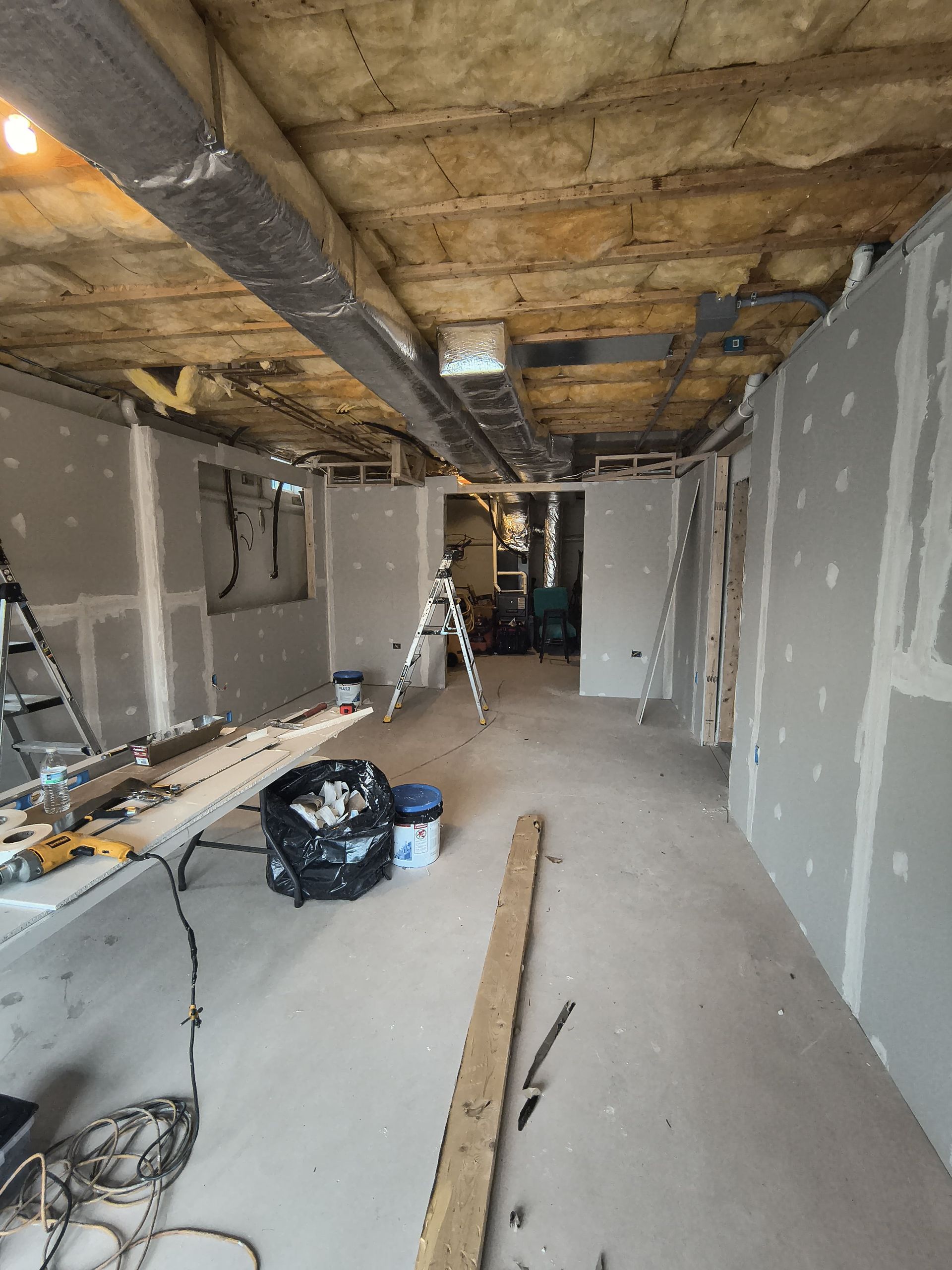 Interior view of a room under construction with exposed ceiling, drywall, and tools.