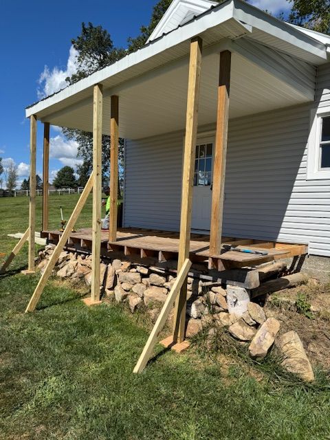 Porch under construction with wooden beams, support braces, and stone foundation.