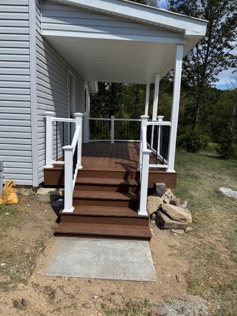 Front porch with stairs and railing, brown deck, white columns and trim, gray siding, and a concrete path.