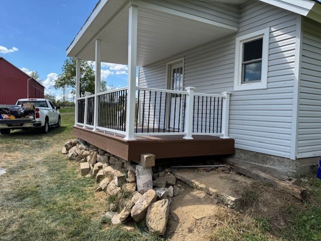 Newly constructed porch on a house with white railing, brown deck, and stone base in a grassy yard.