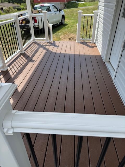 Brown composite deck with white railing and black metal spindles on a porch. A white truck is in the background.