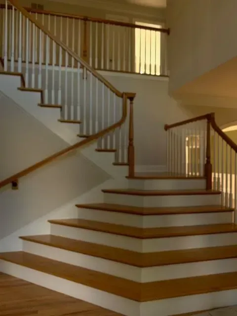Wooden staircase with white risers and railing, brown handrail. Interior view.
