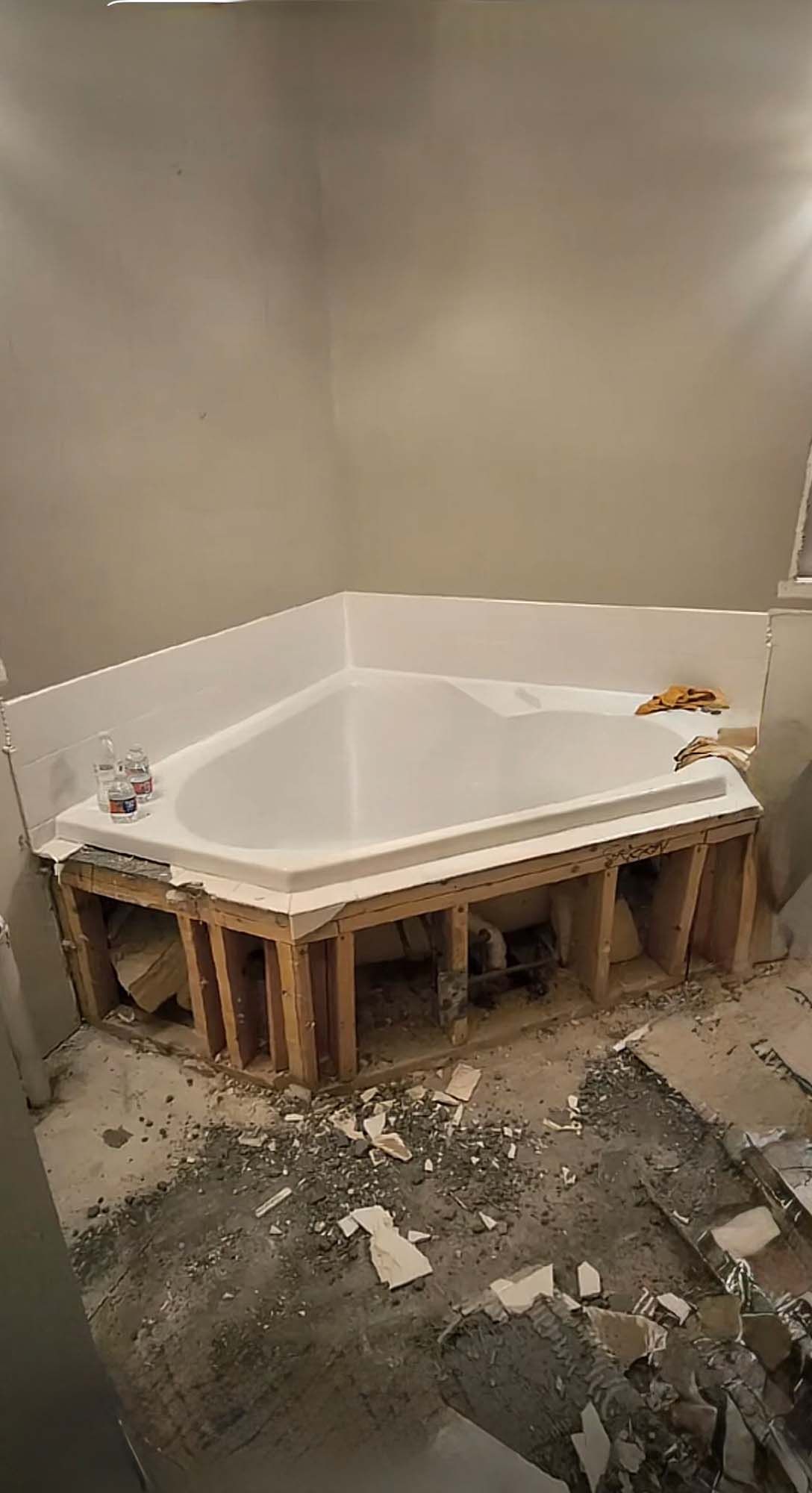 Bathroom under construction, corner soaking tub installed on a wooden frame. Debris on floor.