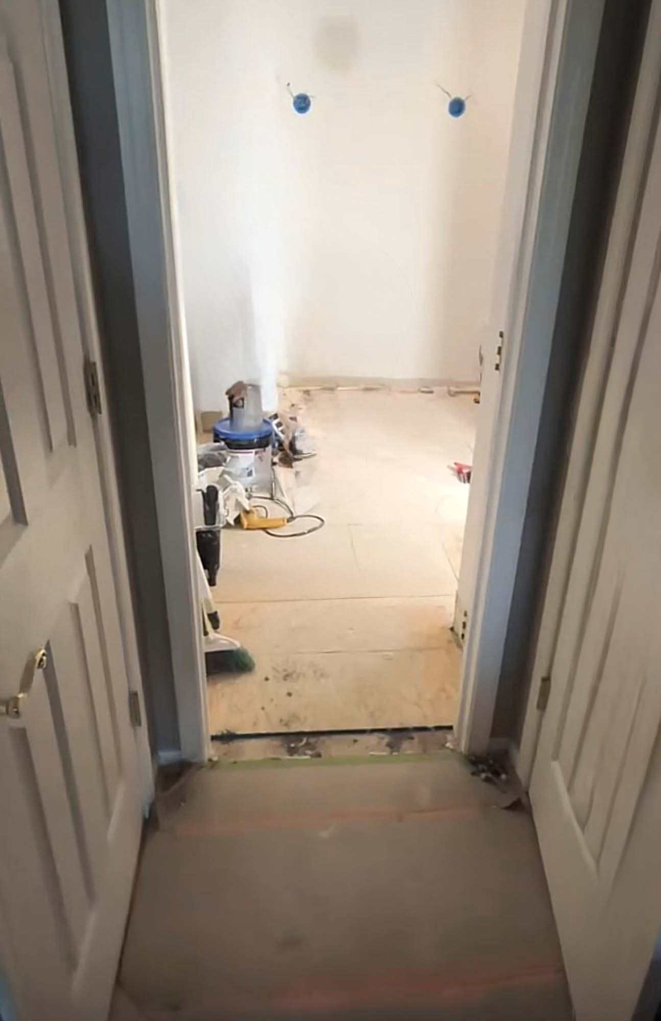 Open doorway into a room under construction with tools and unfinished flooring. White doors frame the view.