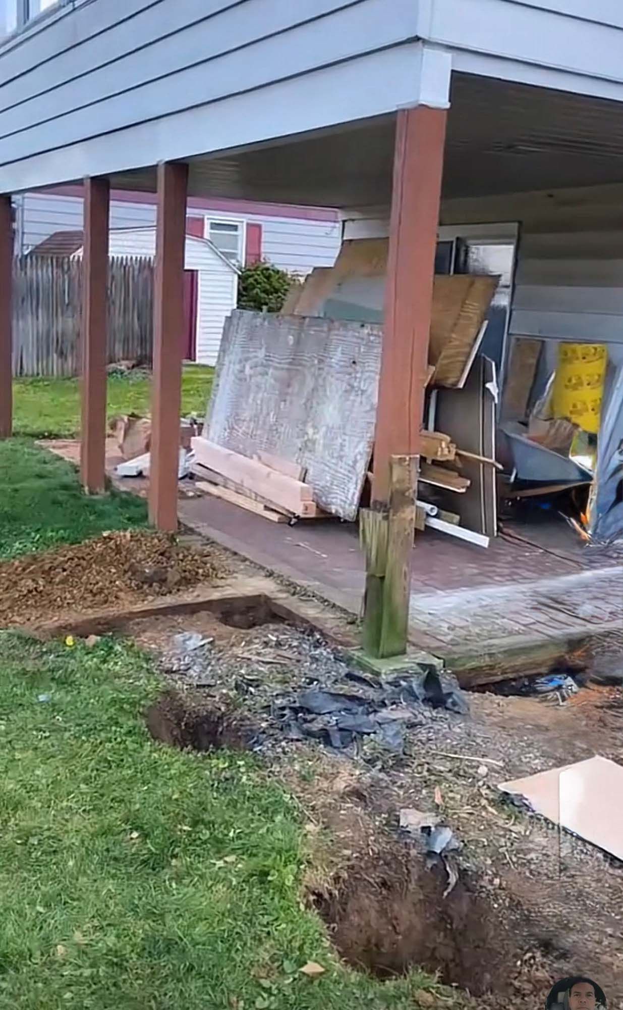 Underneath a deck, a construction site with piles of wood and two dug holes in the yard.