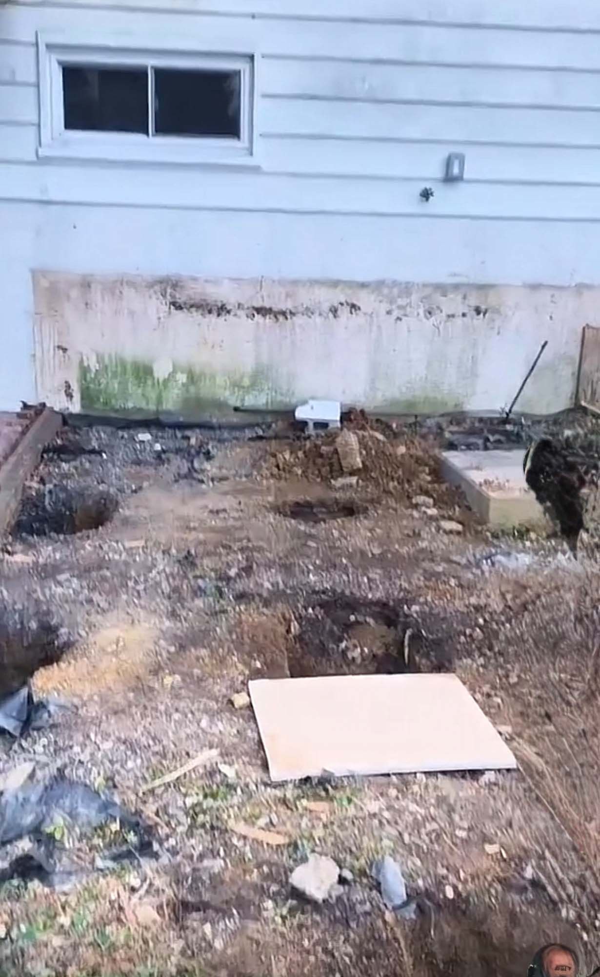 Excavated backyard with dirt, holes, and a partial house. A white square is on the ground.