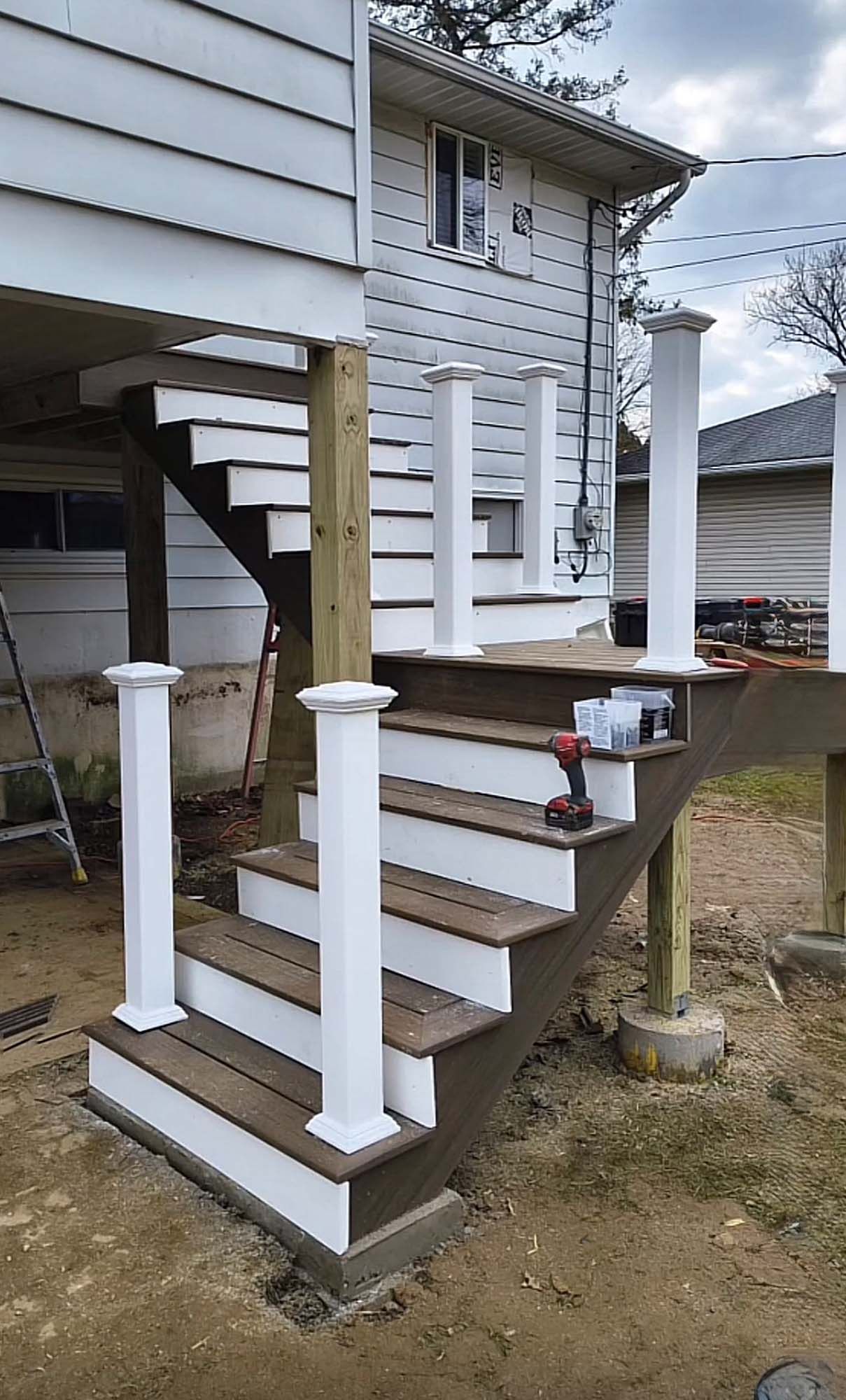 Staircase leading up to a deck attached to a house; composite brown steps, white pillars, outdoor setting.