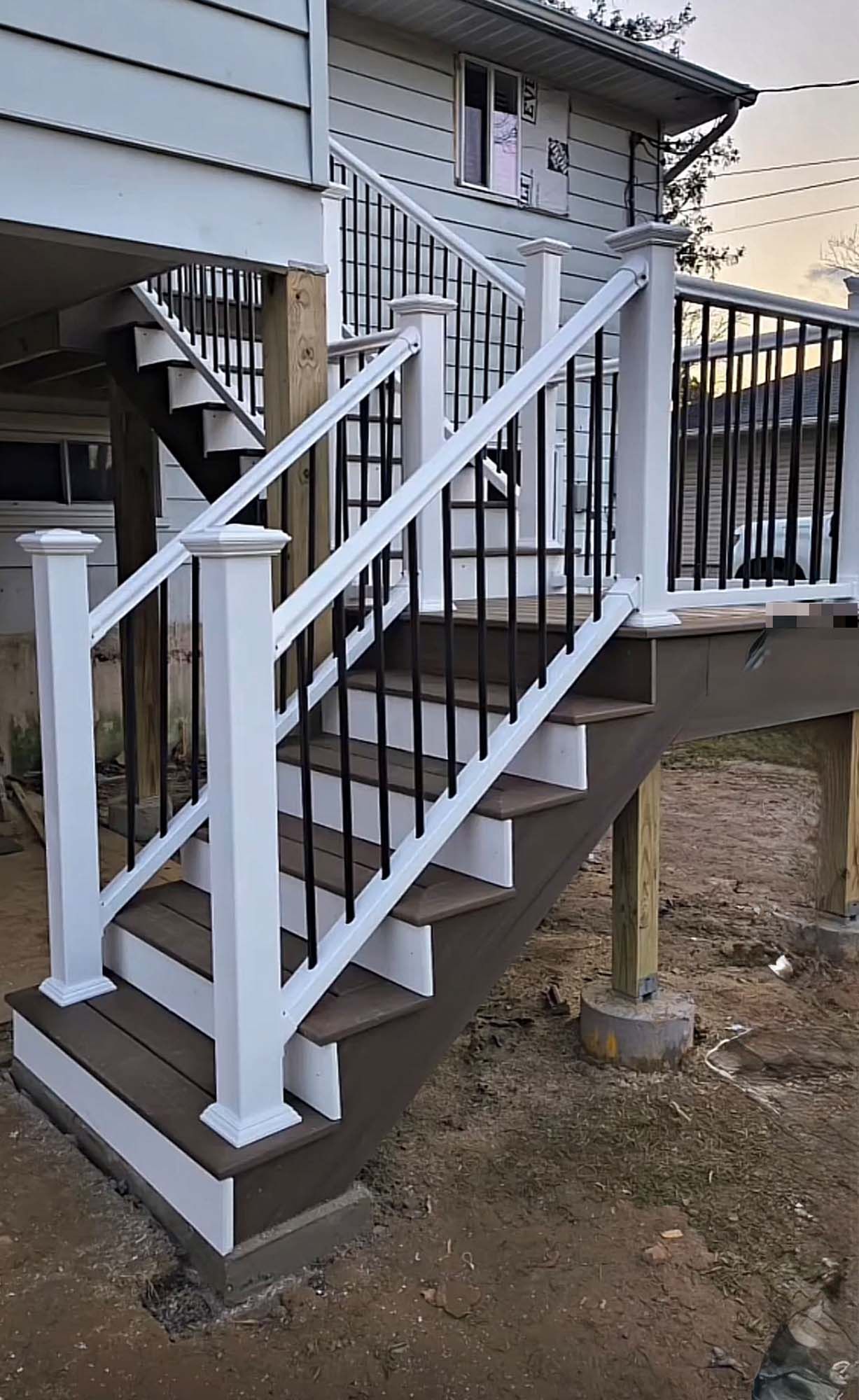 Staircase with white posts, brown steps, and black railings leading to a deck on a house.