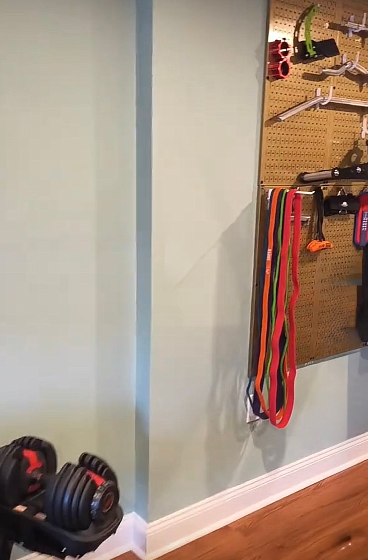 Dumbbells, resistance bands, and other workout equipment arranged on a wall in a home gym setting.