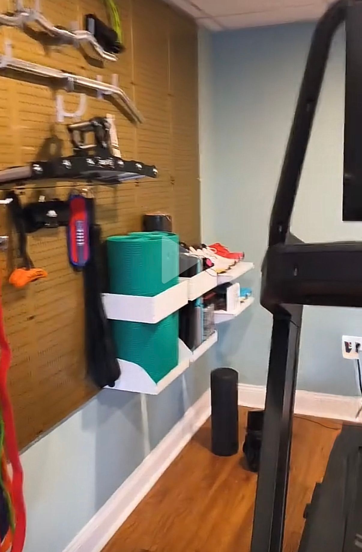 Home gym with treadmill, wall-mounted storage, and wooden floor.