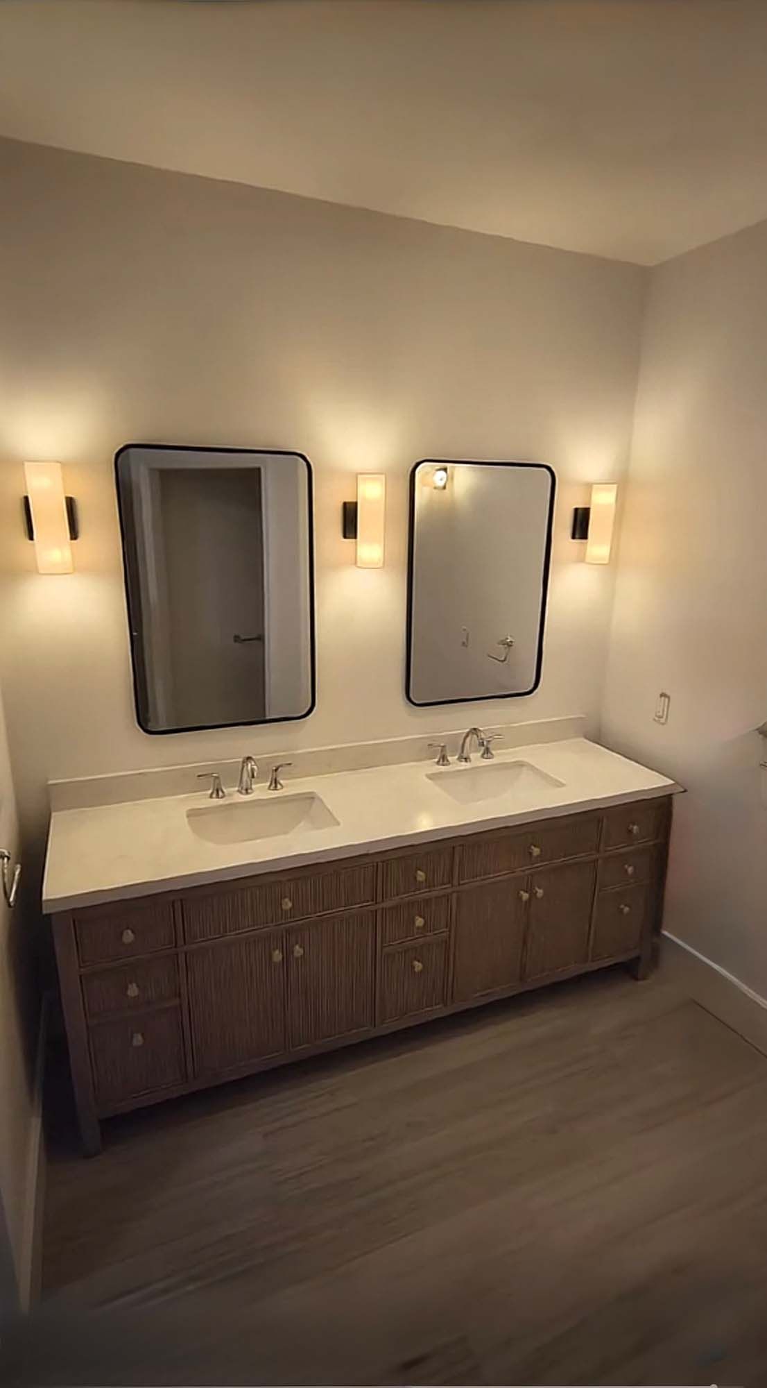 Bathroom with a double vanity, mirrors, and sconce lighting.