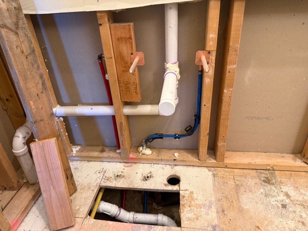 Plumbing partially installed in a bathroom wall during renovation; pipes, studs, and open floor space visible.
