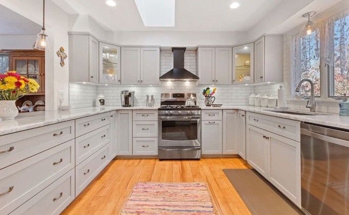 U-shaped white kitchen with stainless steel appliances, light wood floors, and a colorful rug.