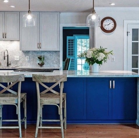 Kitchen with blue island and light gray cabinets, wooden stools, and floral arrangement.