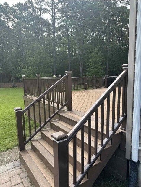 Wooden deck with stairs, brown railing, and light brown decking, in a backyard setting.