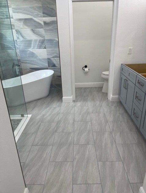 Bathroom with gray floor tiles, white tub, blue and gray shower tile, and light blue cabinets.