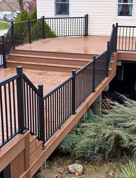 Brown wooden deck with black railings and steps leading up to a house with white siding.