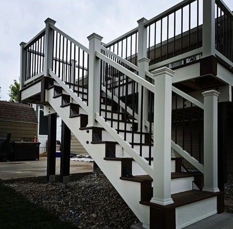 White and brown deck stairs with black railings leading to a second-story deck, set outdoors.