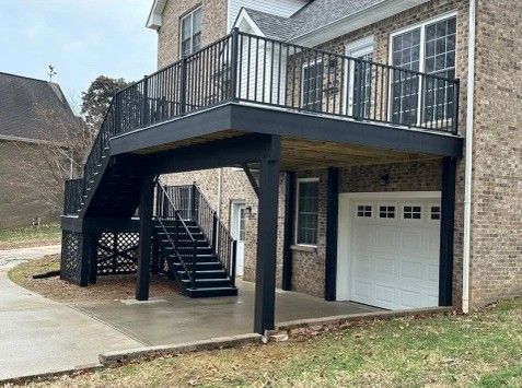 Black deck with stairs over a garage, attached to a brick house.