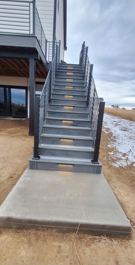 Outdoor staircase with gray steps and black railings. Concrete path in front.
